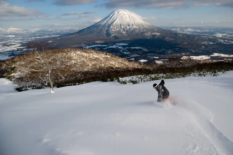 Photo of a snowboarder riding deep powder in Niseko with a stunning view of Mt Yotei in the background