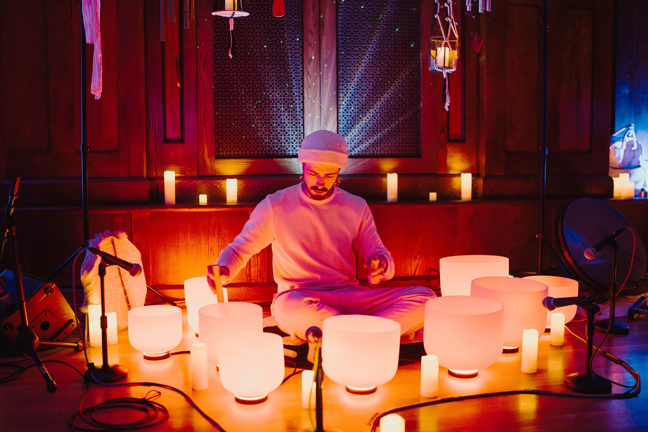 People lying on mats on the floor with candles around in a dark room with colorful lights and projection effects, likely part of a meditation or relaxation session.