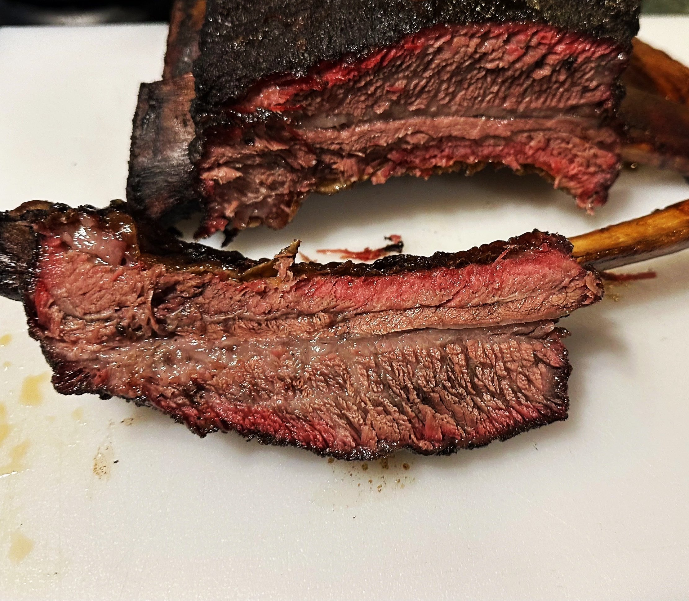 Close-up of cooked beef Dino ribs on a white cutting board, with some meat detached from the bone.