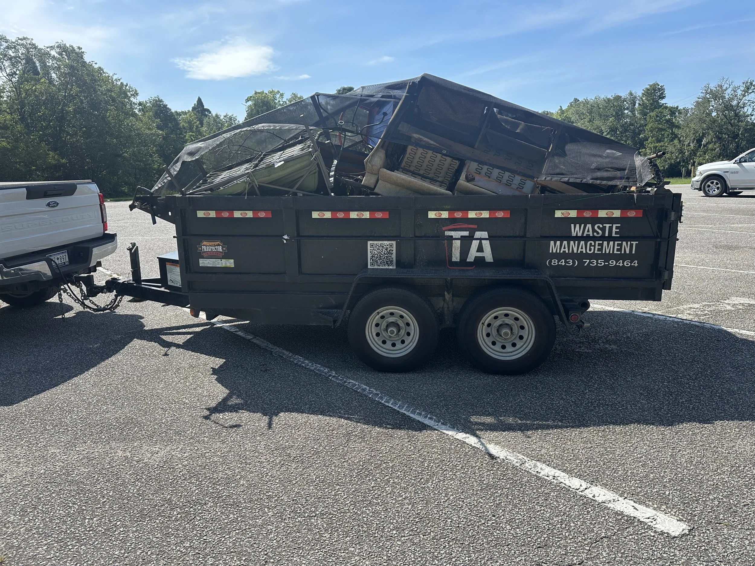 Dump trailer filled with trash being hitched to a pickup truck in a parking lot.