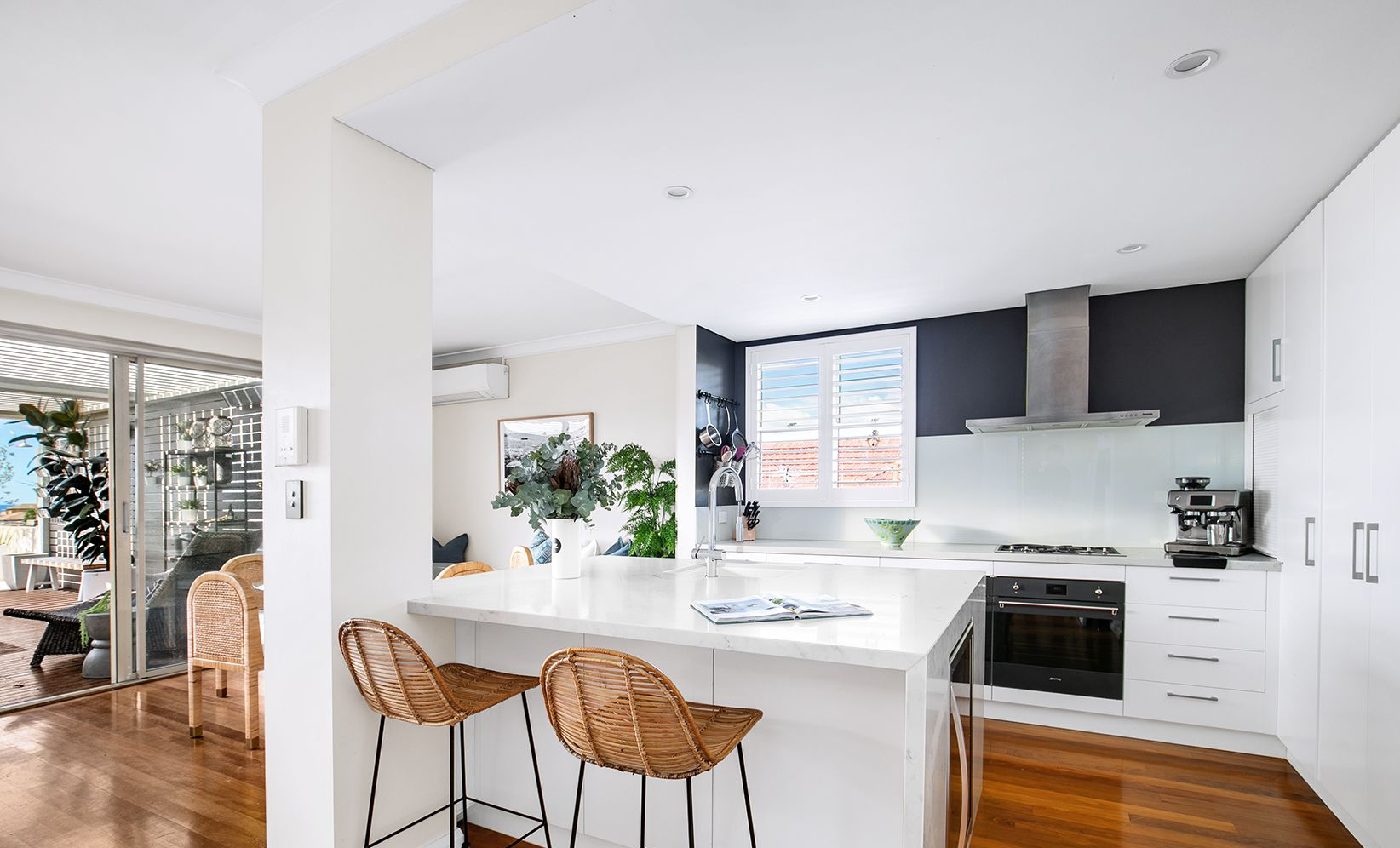 Modern white kitchen with an island, rattan chairs, and a window with shutters