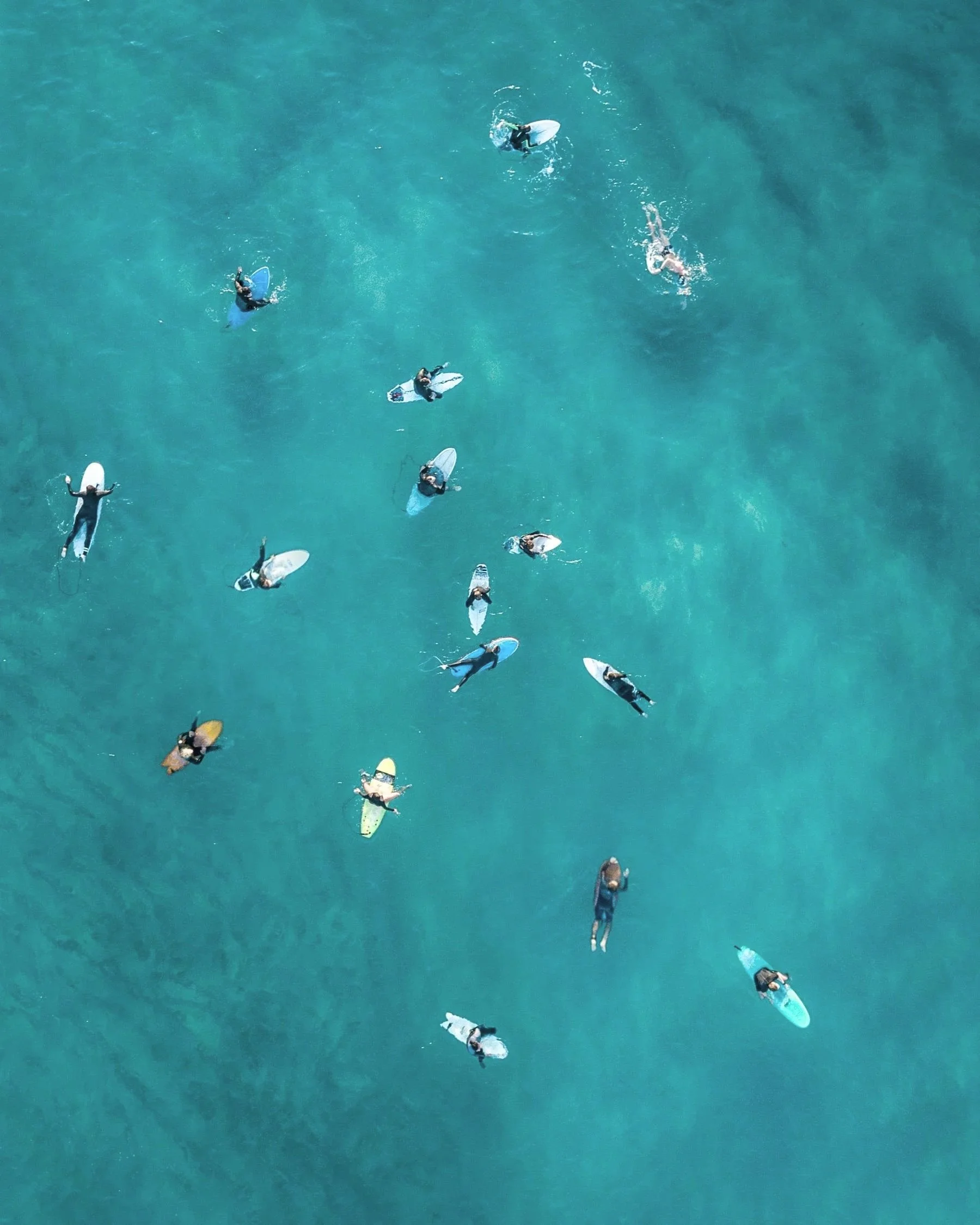 Overhead view of surfers and paddleboarders in the ocean, some on surfboards and others on paddleboards, enjoying a sunny day.