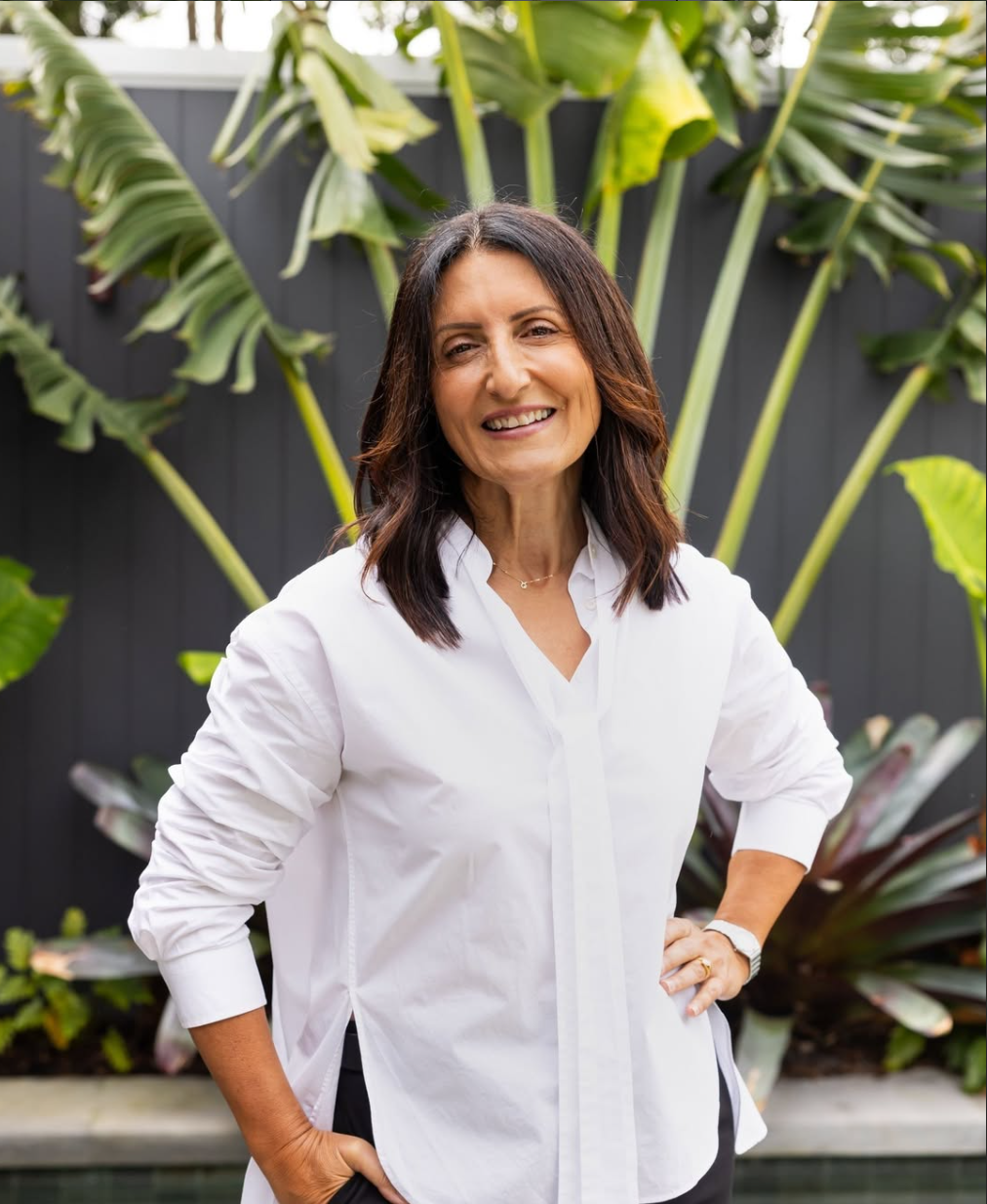 Irene one of the founders of IN Property Agents standing outdoors in front of lush green tropical plants with large leaves, smiling at the camera.