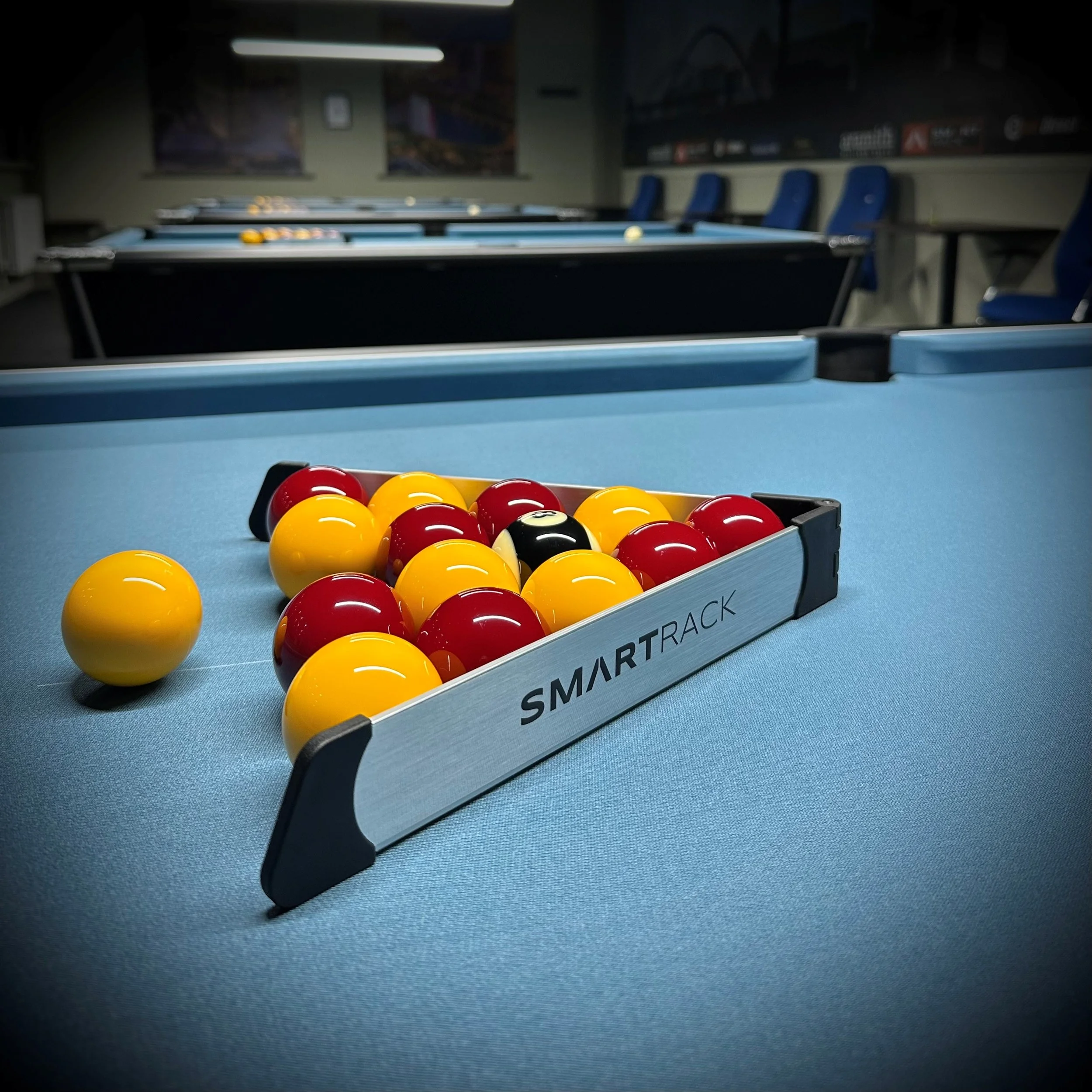 Pool balls arranged on a blue pool table with a sign that reads 'SMART RACK' and blue chairs in the background.