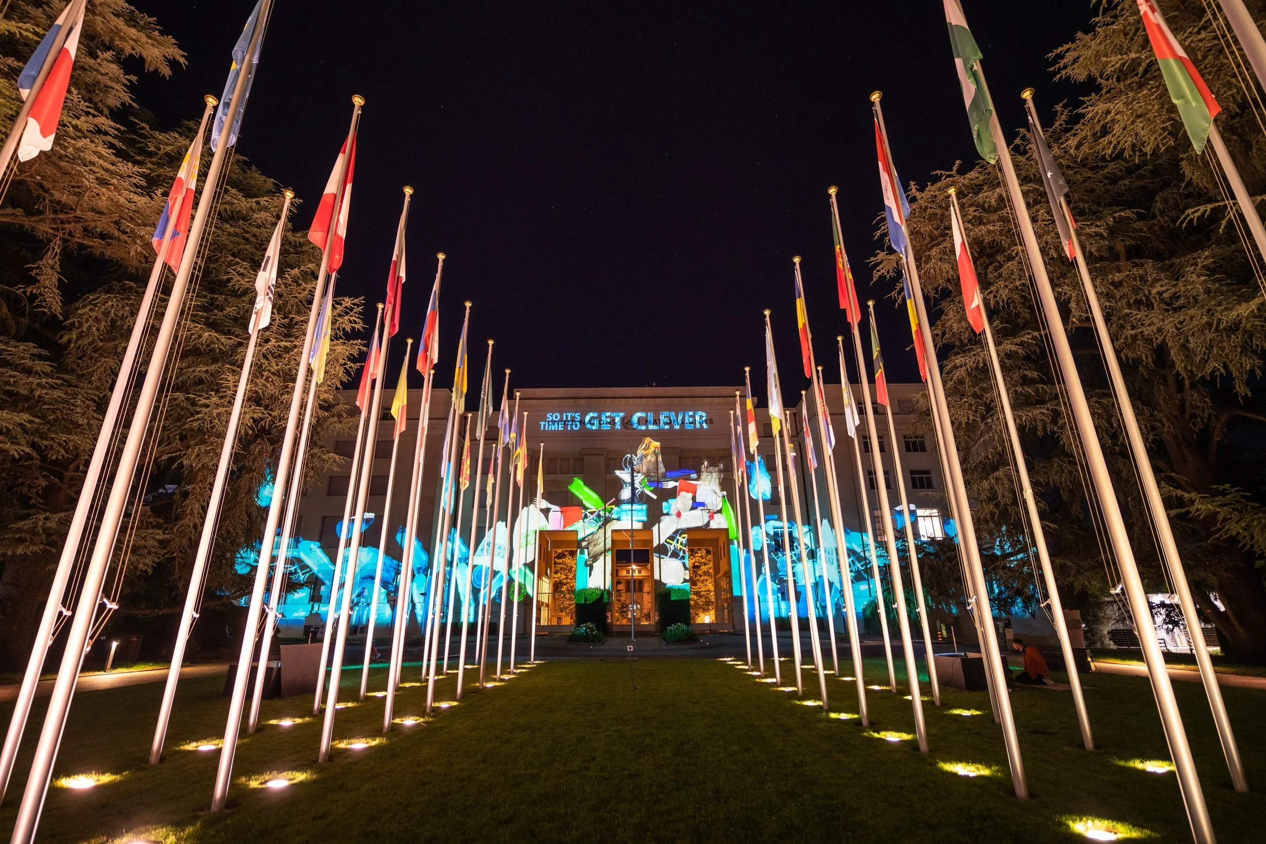UN building with country flags and pieces of plastic projected onto building - Image is taken from UN Plastic is forever film by Heehaw