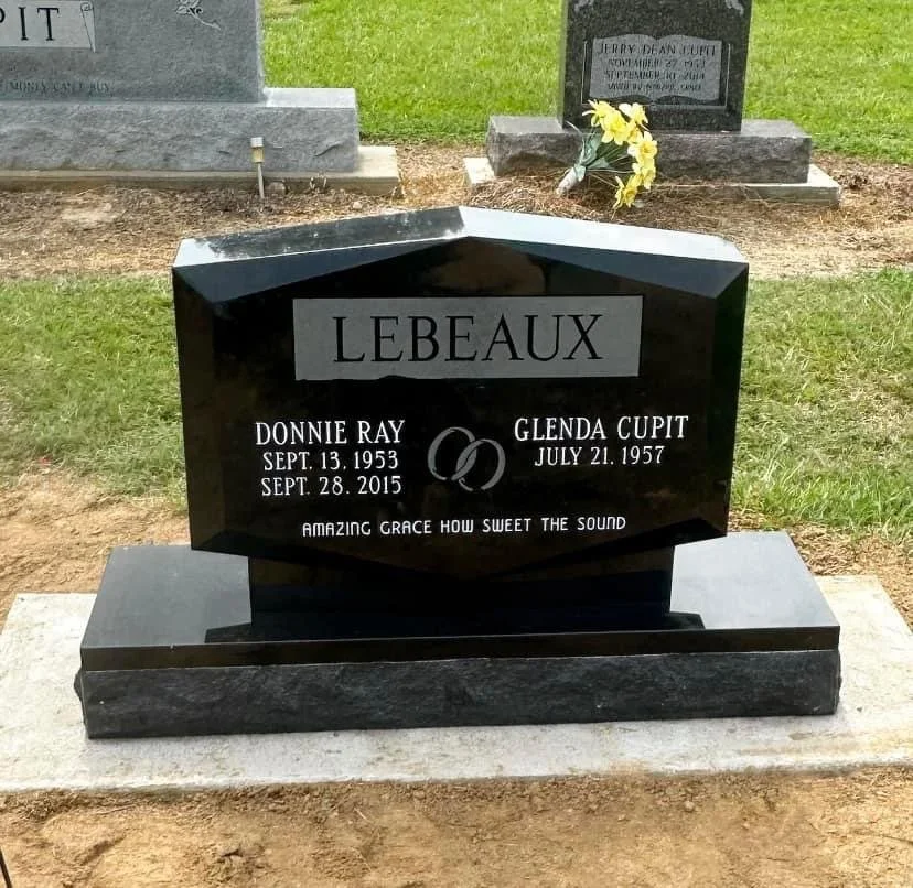 Black granite headstone for Donnie Ray and Glenda Cupit Lebeaux, with their birth and death dates, and a pair of wedding rings engraved between their names. The headstone has the inscription 'Amazing grace how sweet the sound'.