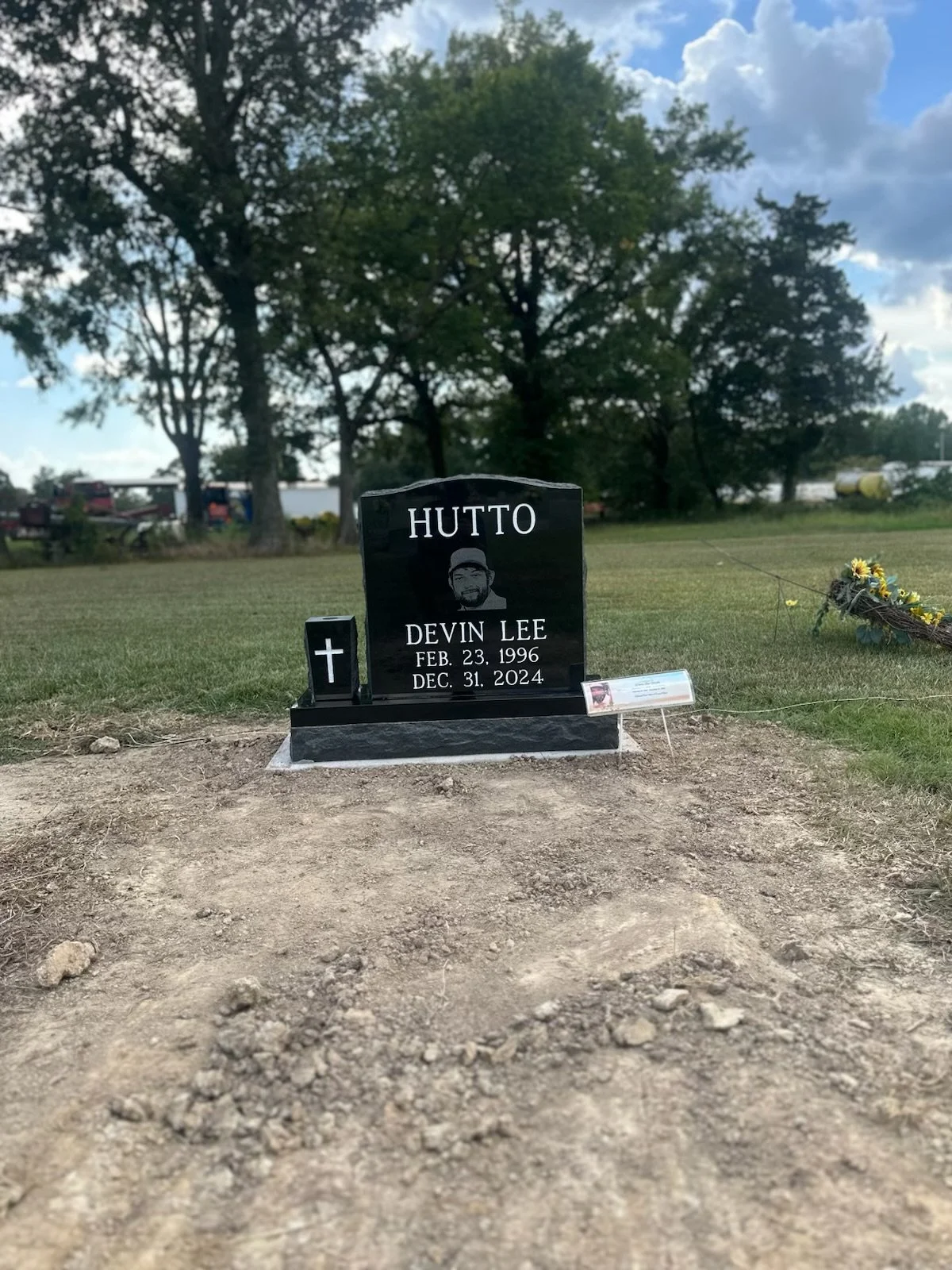 Gravestone for Devin Lee Hutto, born February 23, 1996, died December 31, 2024, with a small black cross and a small image of the deceased.