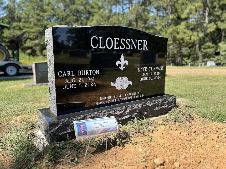 Black granite headstone with white engraved text for Carl Burton and Kaye Tornage, including birth and death dates, located in a grassy cemetery with trees in the background.