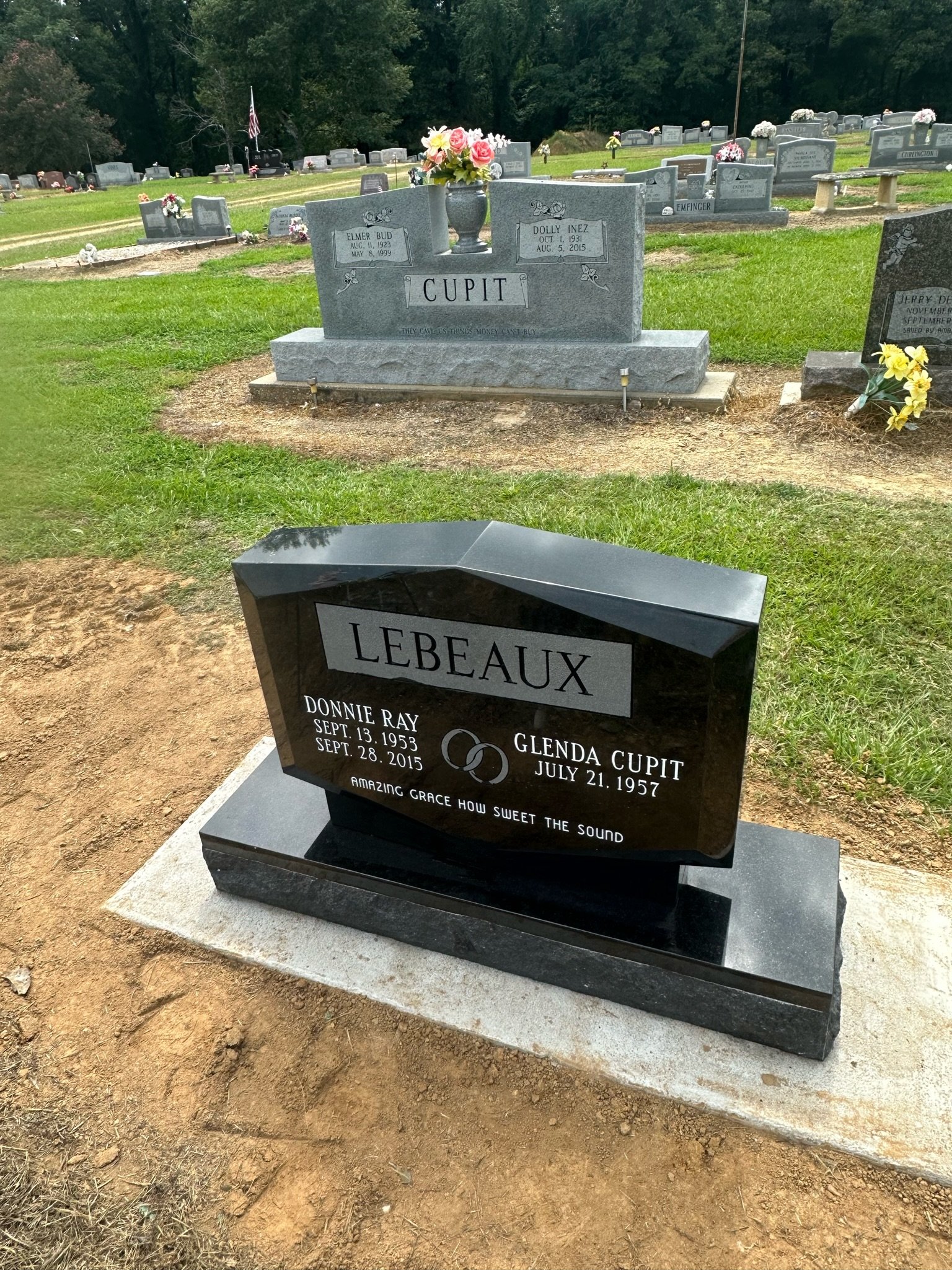 A black polished headstone with the surname 'Lebeaux' engraved, in a cemetery. It has the names Donnie Ray LeBeaux (September 13, 1953 - September 28, 2015) and Glenda Cupit. The headstone also features an engraved wedding ring and the phrase 'Amazin