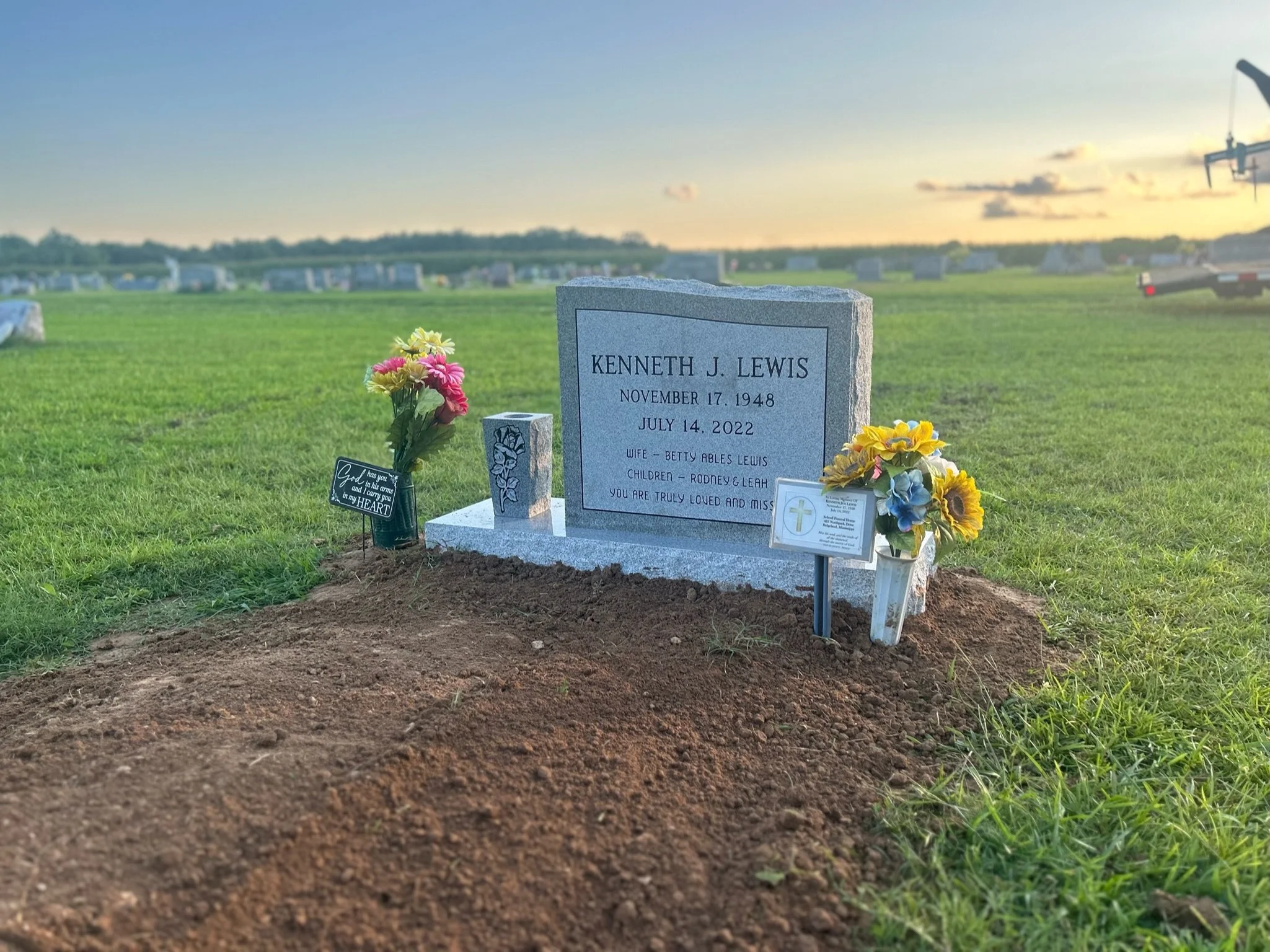Gravestone with flowers and small religious card in a cemetery at sunset.