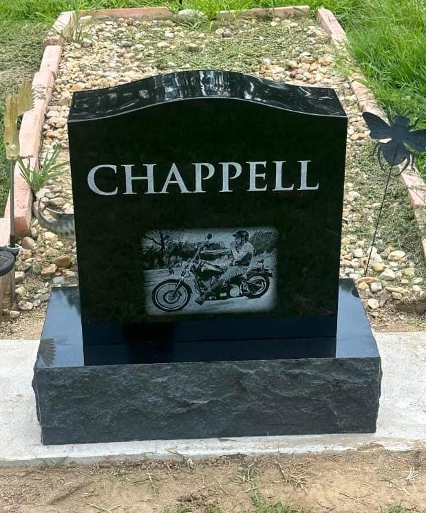A black granite headstone with the name 'CHAPPELL' engraved on it, featuring a black and white photograph of a man sitting on a motorcycle.