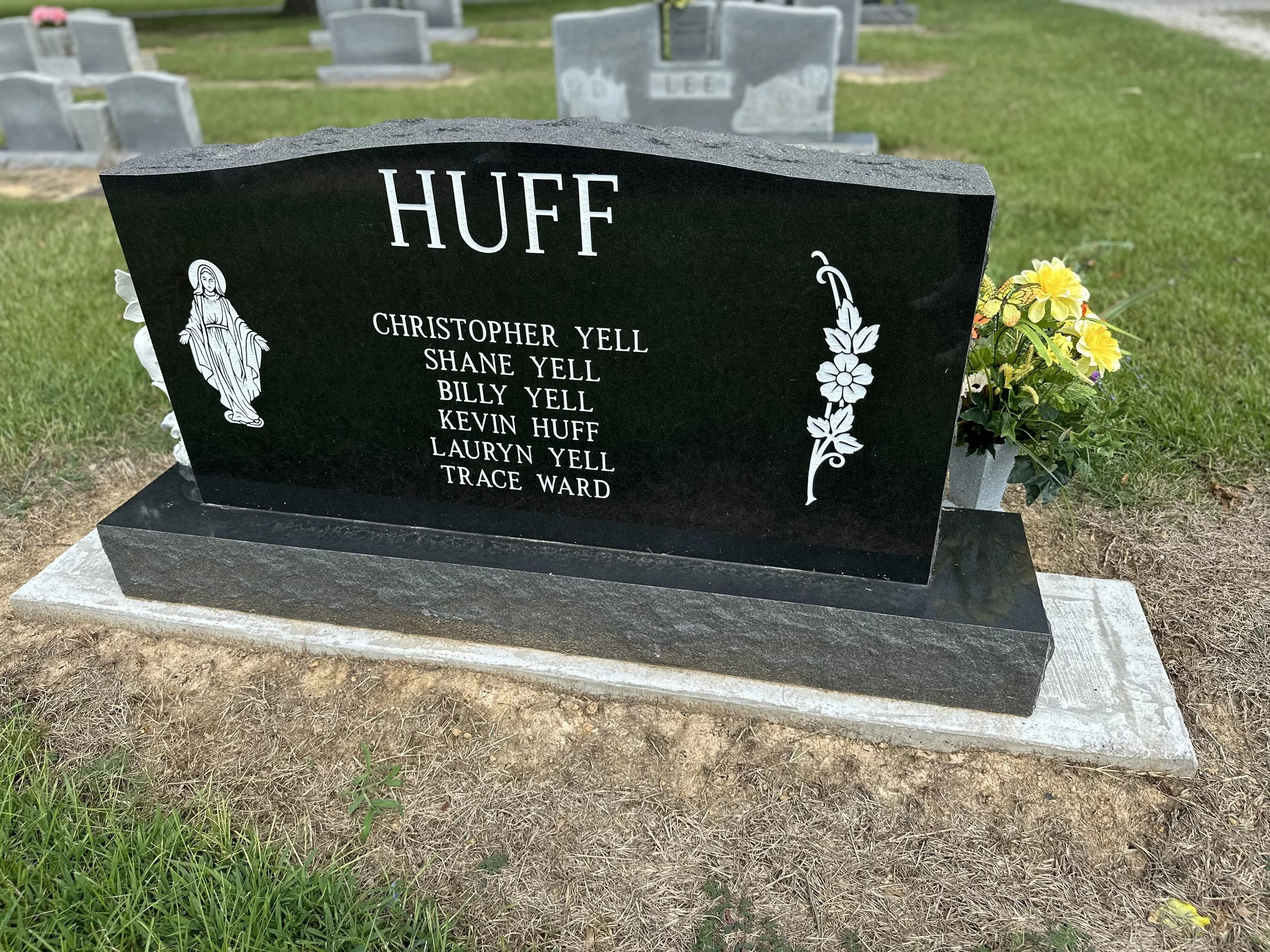 A black granite gravestone with the surname "Huff" at the top, honoring seven individuals including Christopher Yell, Shane Yell, Billy Yell, Kevin Huff, Lauryn Yell, and Trace Ward. The gravestone features an illustration of the Virgin Mary on the l
