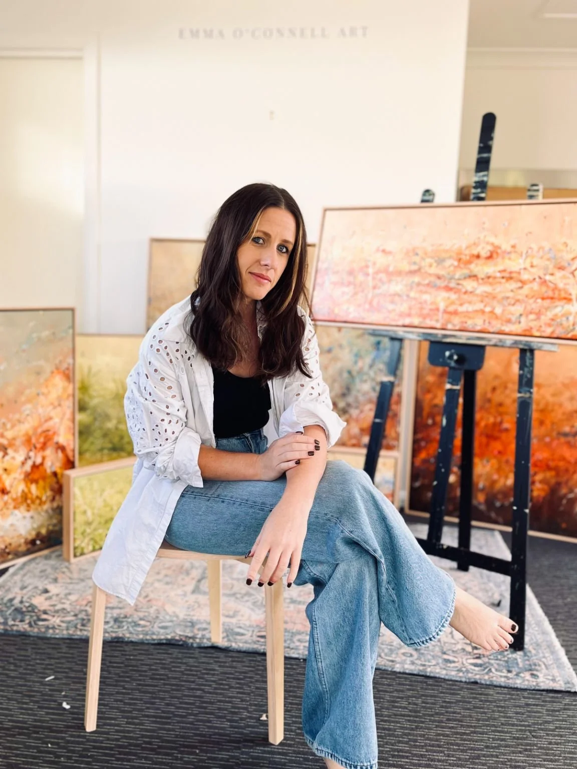 Artist Emma O'Connell sat on a stool in front of her paintings.