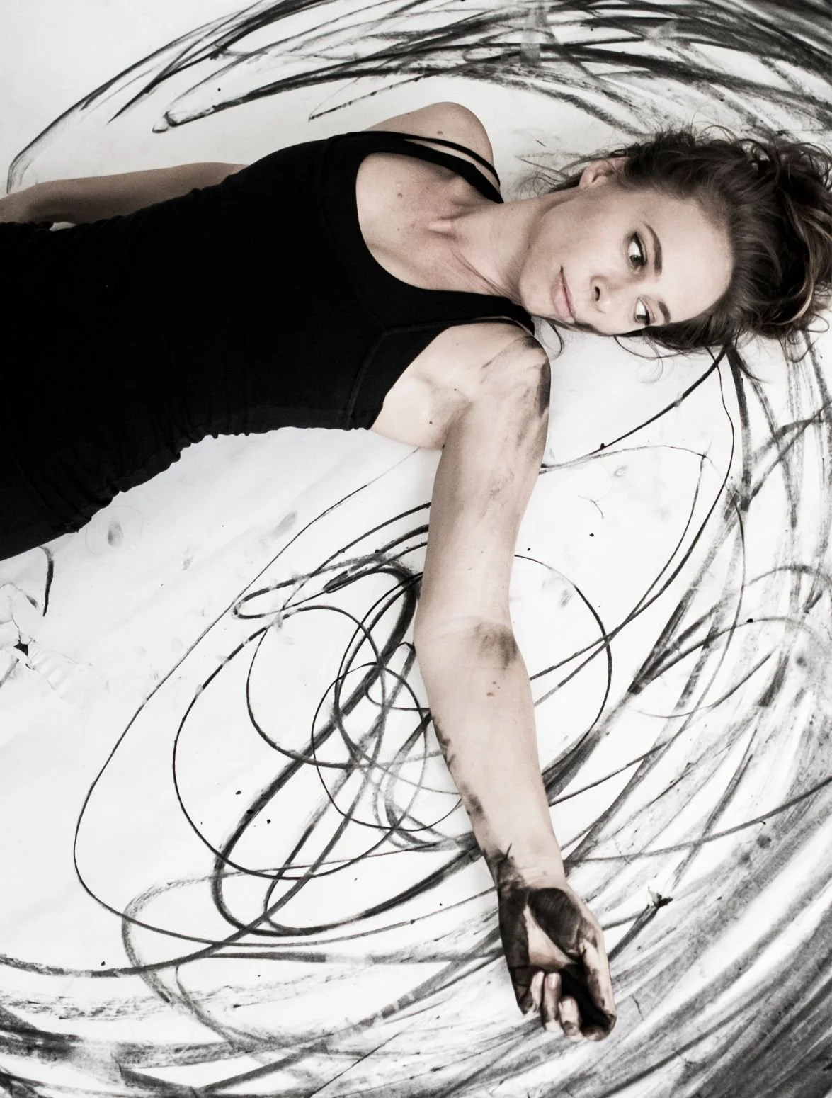 Artist Kylian Martin lying on a canvas covered in charcoal marks.