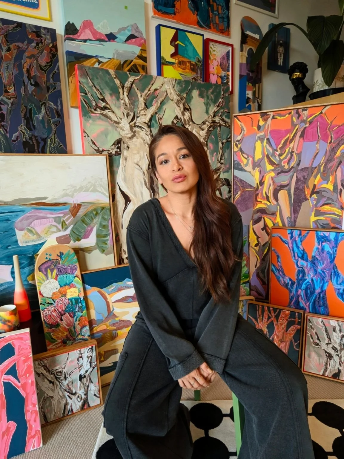 artist Bravo Domino wearing black and sat in front of many of her artworks