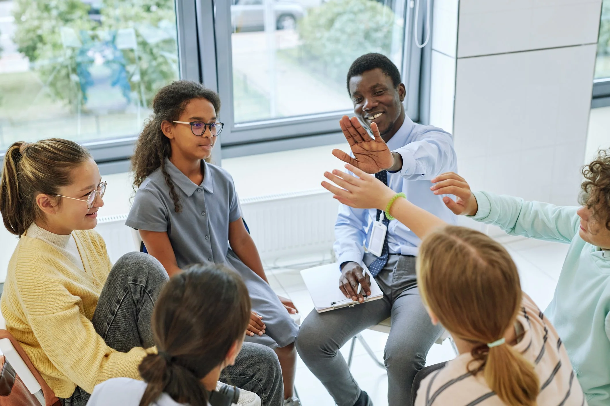 Black male group therapist sitting in a circle with a group of middle school-age teens.