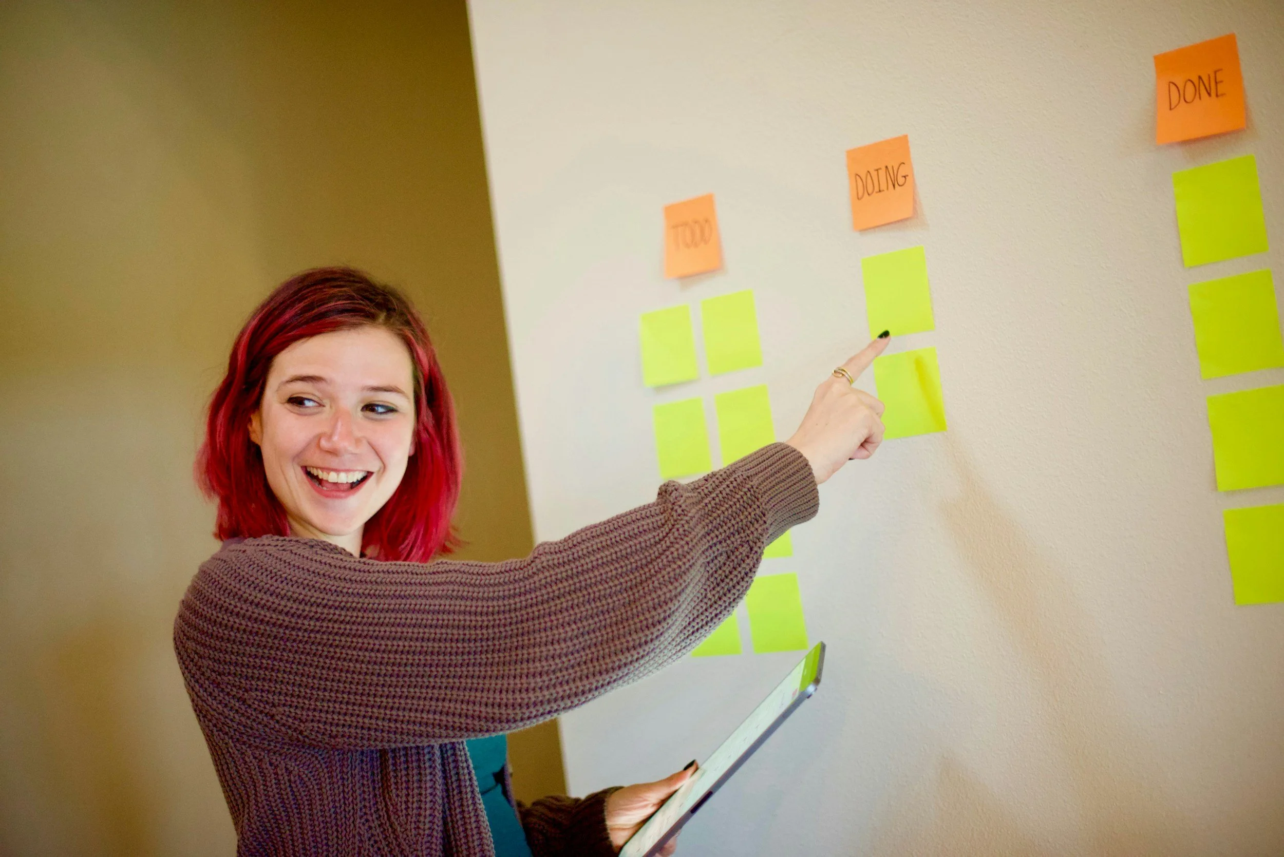 Teacher with red hair pointing to the board while smiling at students.