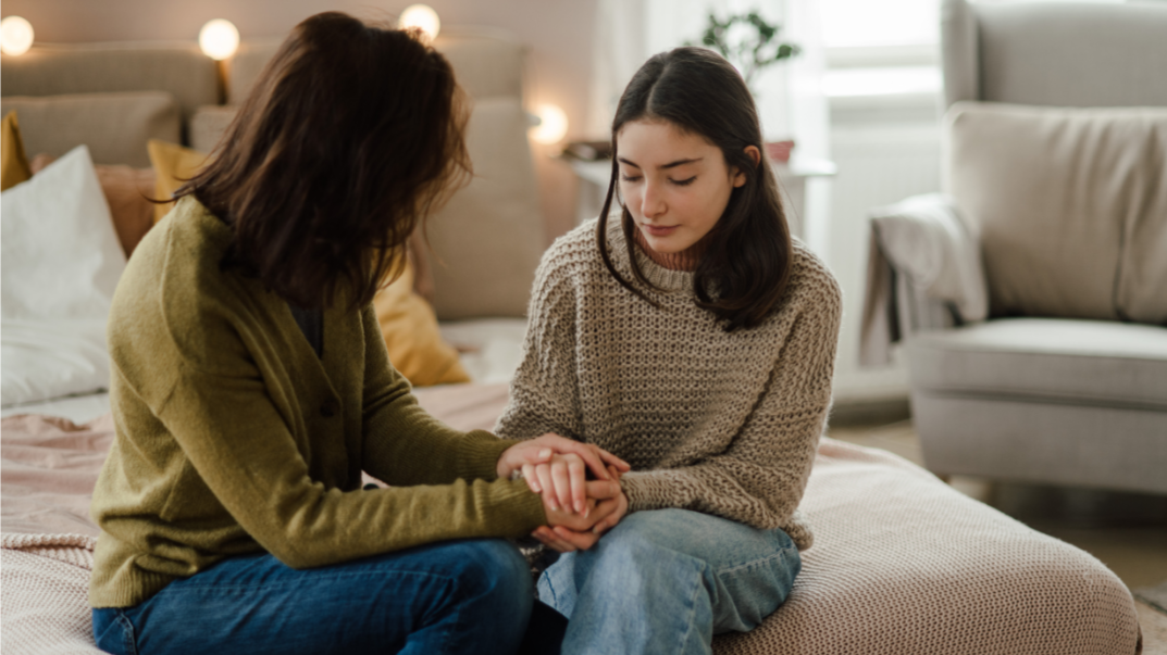 Teen daughter sharing problems with her mother, holding hands.
