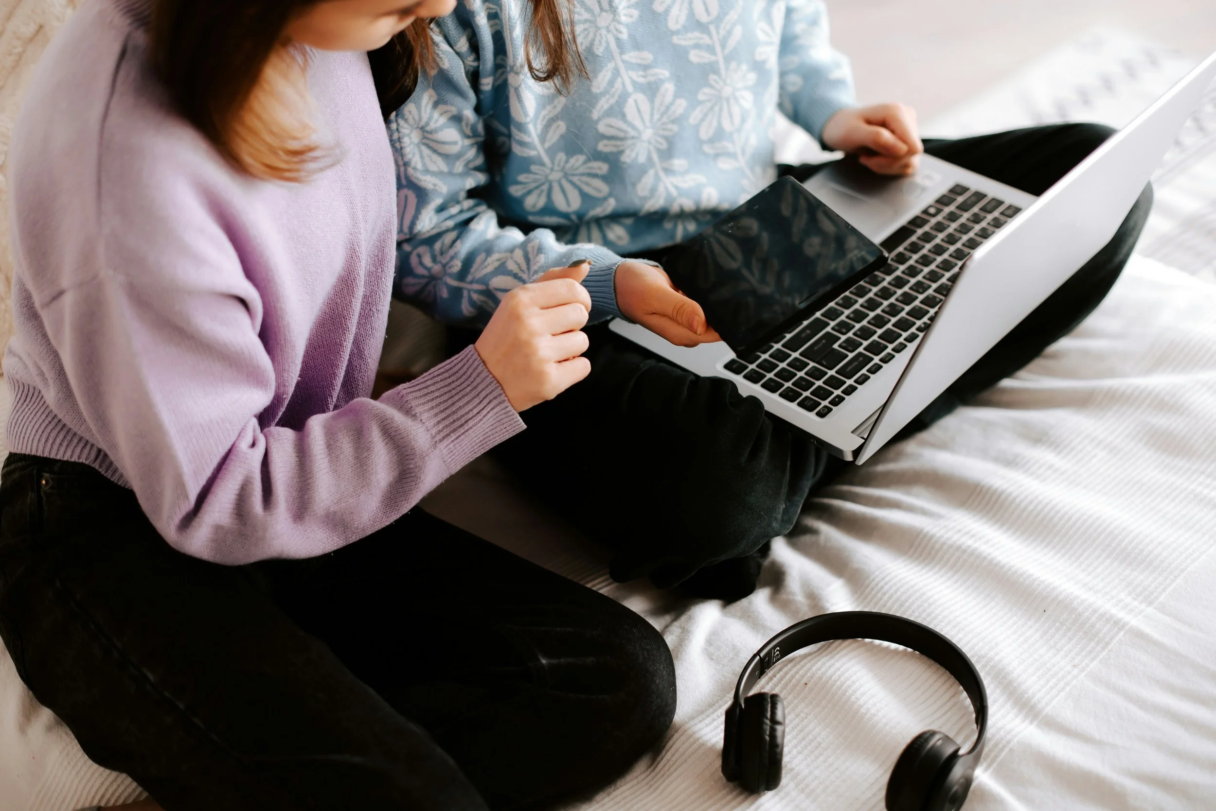 Two people sit together on a bed, looking at a laptop together