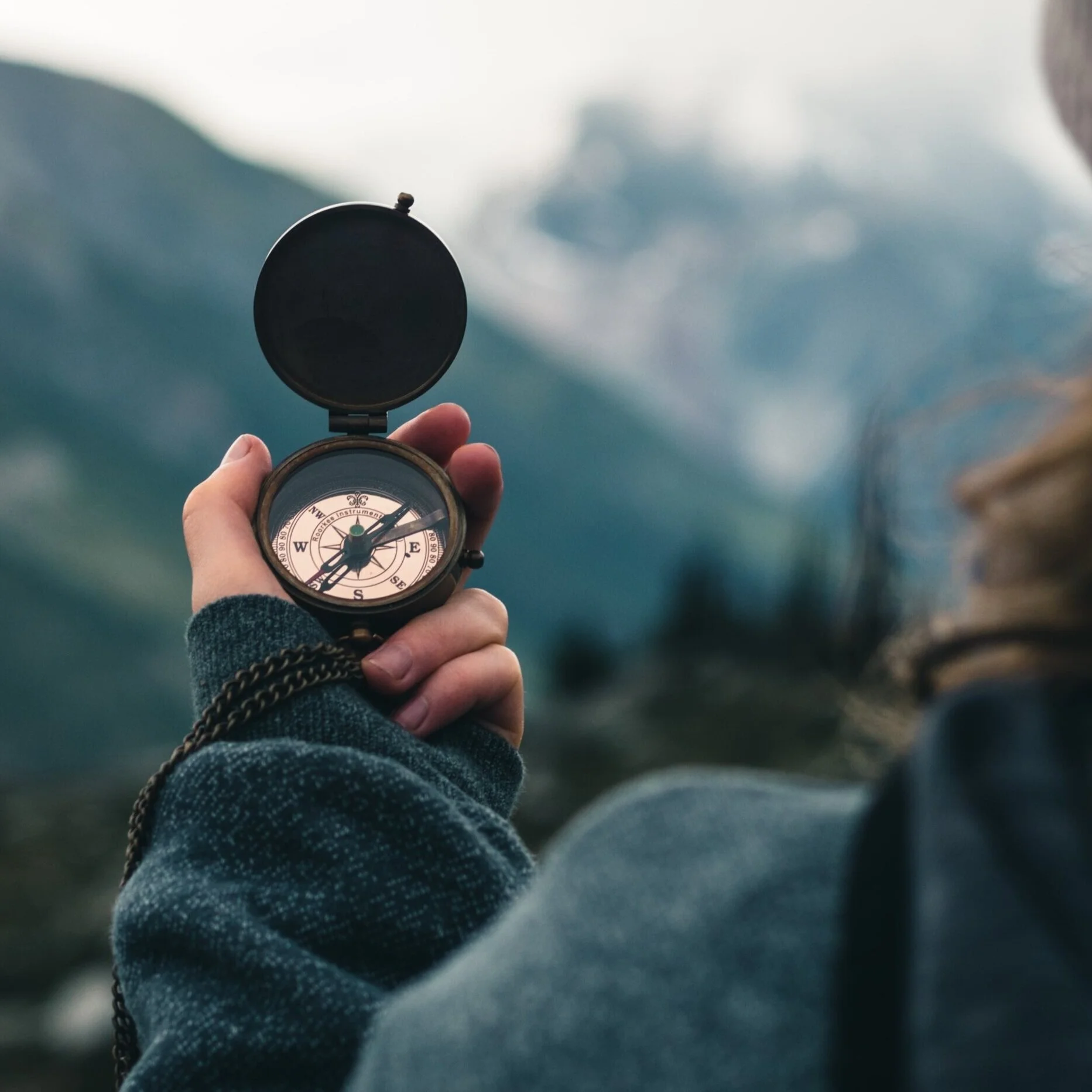 Woman looking out over mountains, holding a compass in her left hand