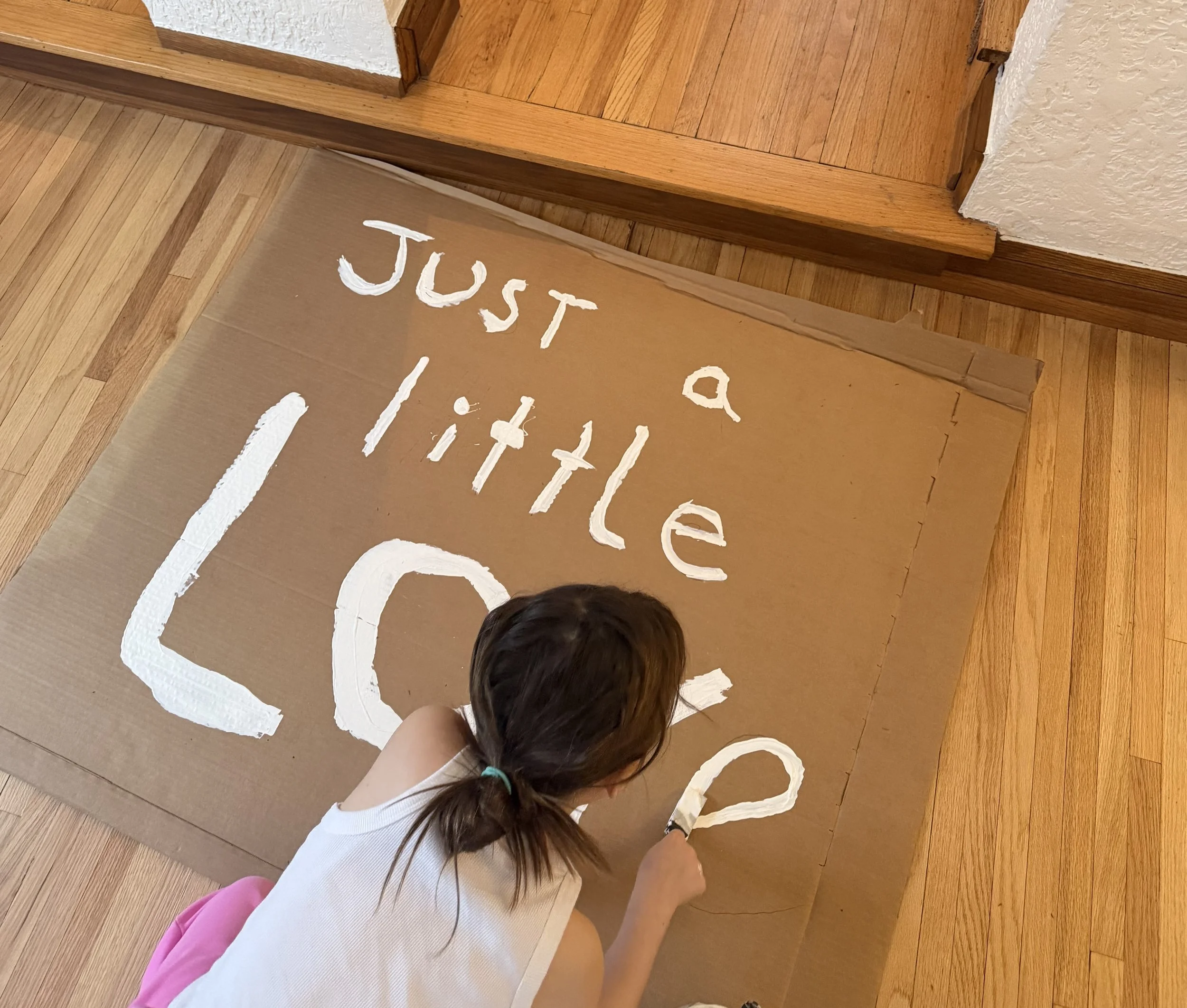 My daughter making a sign that reads "Just a little love" - Photo by Jackie Colburn