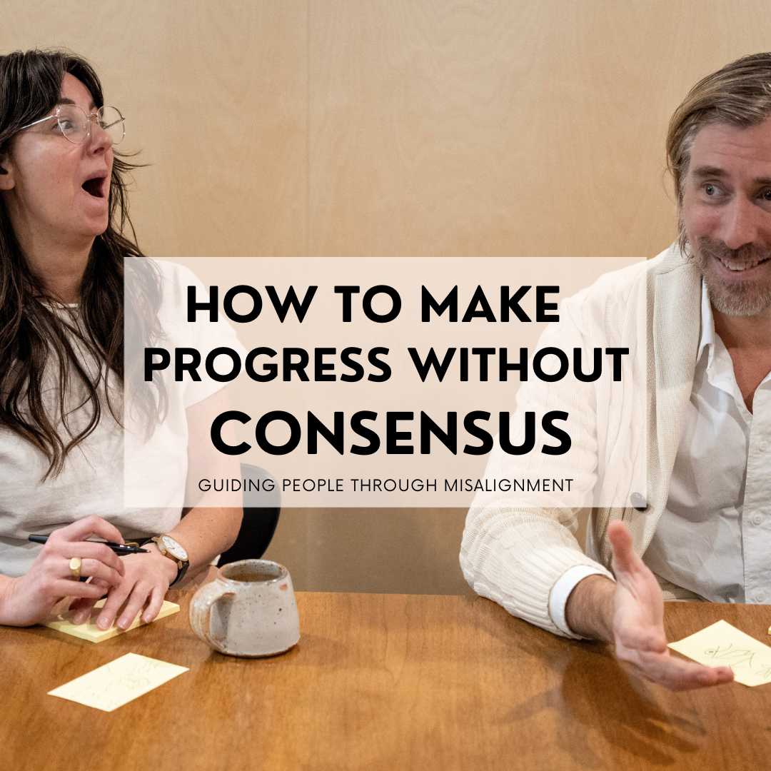 Woman laughing at man next to her while at conference room table.