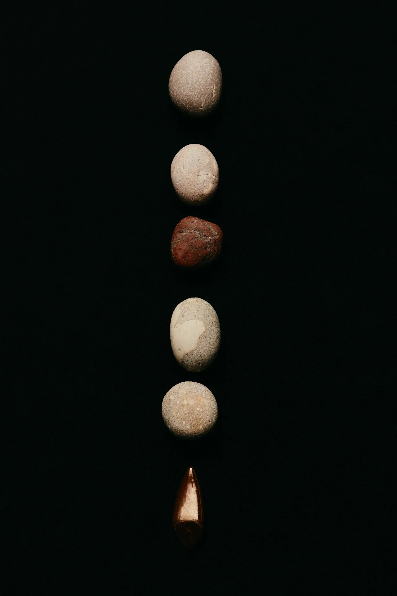 Line of various stones and a copper-colored metallic object on black background