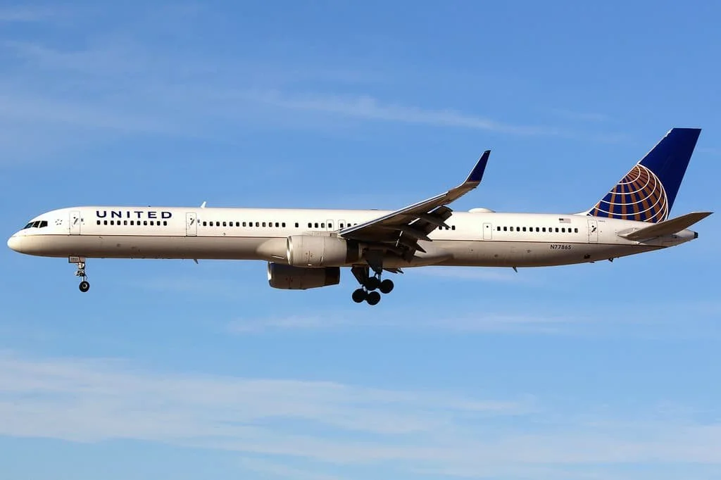 A United Airlines 757 flying in the sky against a blue sky with some clouds.