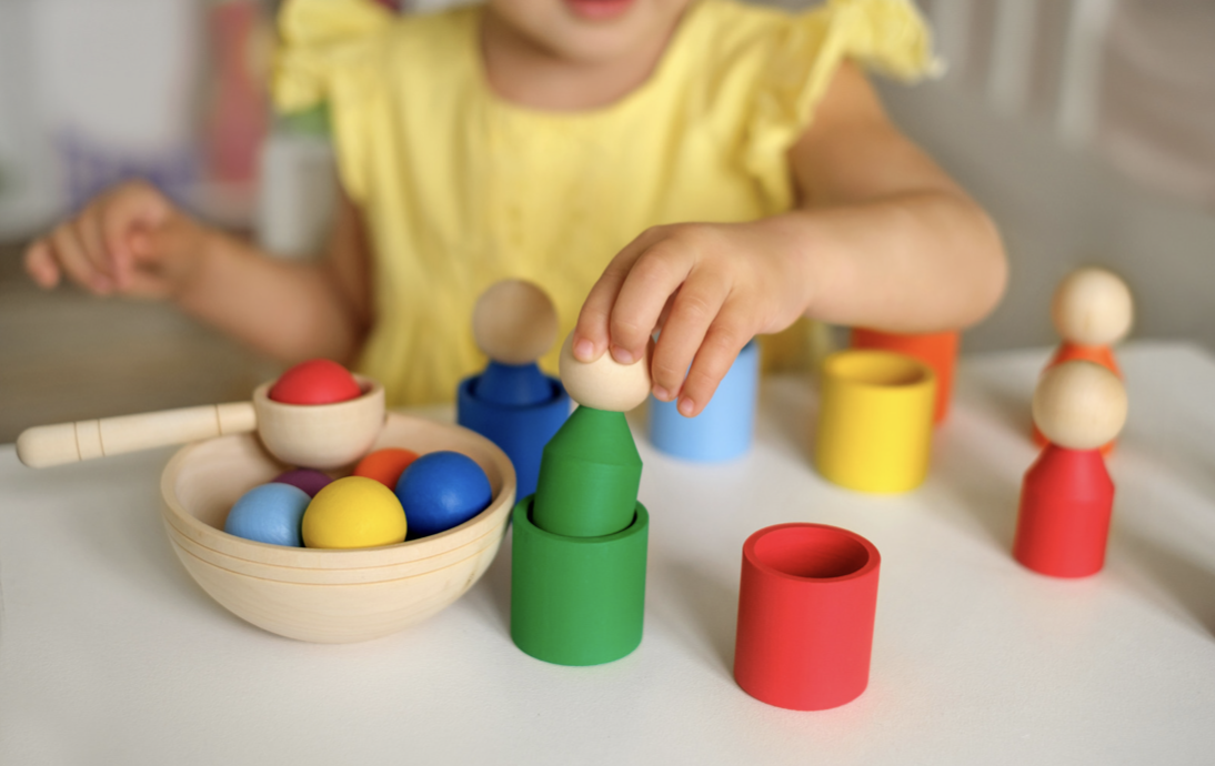 Child playing with colorful wooden stacking toys and a bowl of balls.