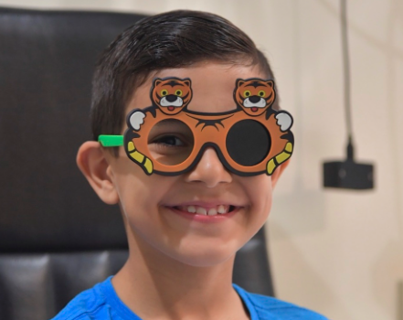 Child wearing fun tiger-themed eyeglasses in an office setting.