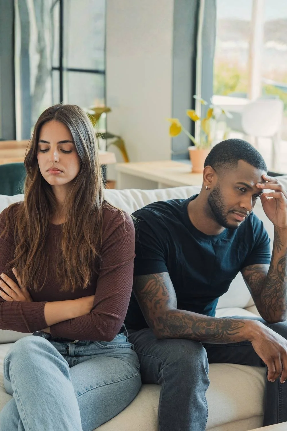 A woman and a man sitting on a sofa, both appearing upset and frustrated, with arms crossed and hands on their heads.