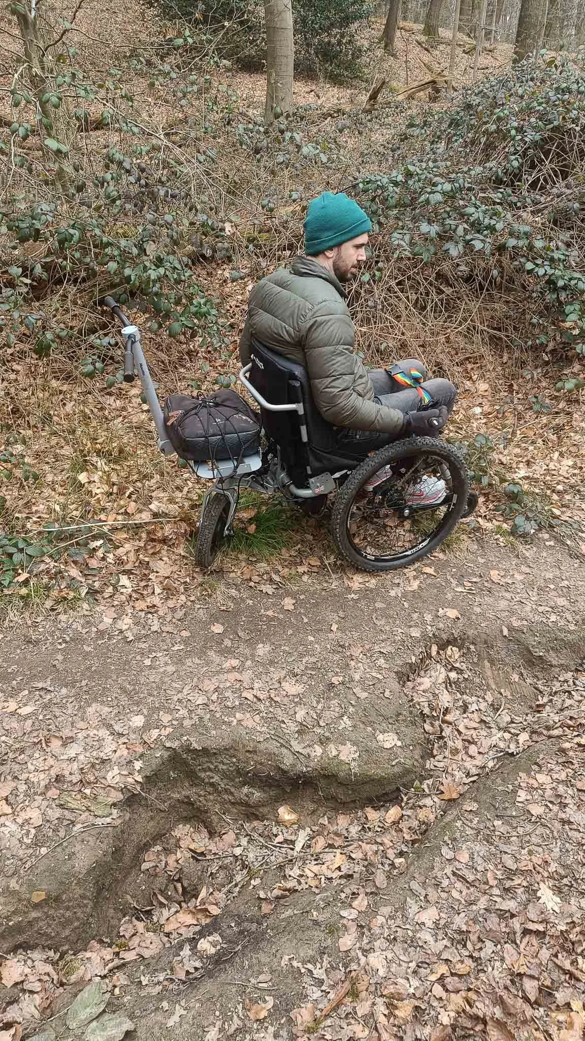 Man in rolstoel op een bosweg met omgevallen boom ontbrekend door de kracht van een boom die is omgevallen.