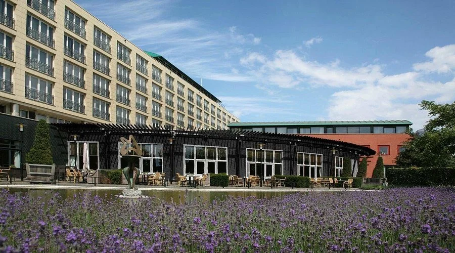 Een modern gebouw met een buitenterras en tuin met bloemen, onder een blauwe lucht met enkele wolken.