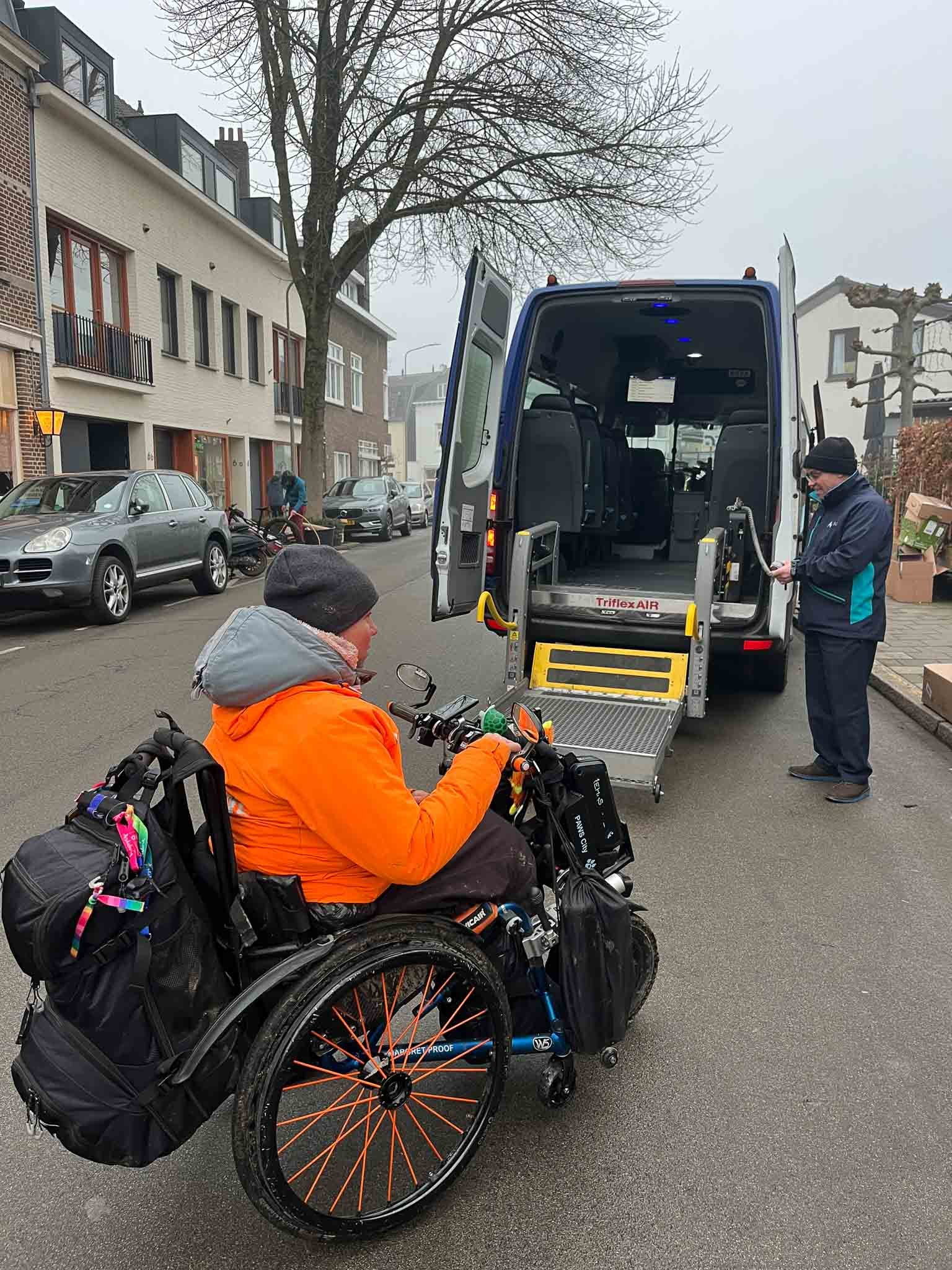 Een persoon in een rolstoel wacht terwijl een andere persoon zich voorbereidt om in een bus te gaan die speciaal is aangepast voor rolstoelgebruikers.