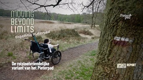 Vrouw in een rolstoel met een driewielige elektrische fiets op een modderig en besneeuwd pad, omgeven door kale bomen en weiden.