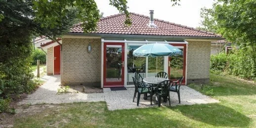 Toegankelijke accommodatie aan het Pieterpad. Een kleine woning met een tuin, tafeltje en stoelen met een parasol, omgeven door groen.
