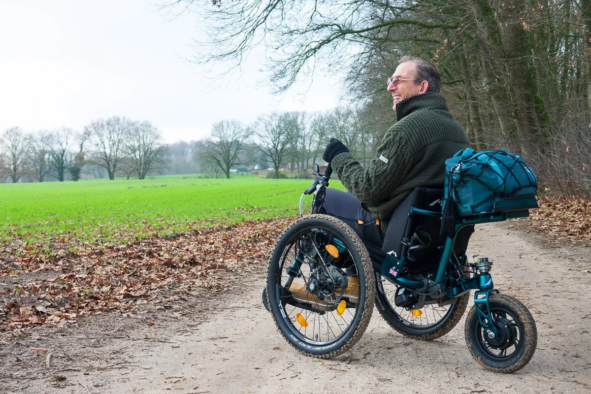 Vrouw in een rolstoel die in een bos wandelt met zonlicht dat door de bomen schijnt.