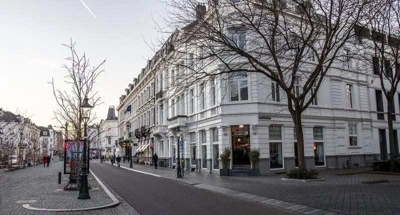 Een rustige straat in een stad met witte historische gebouwen, bomen en straatverlichting.