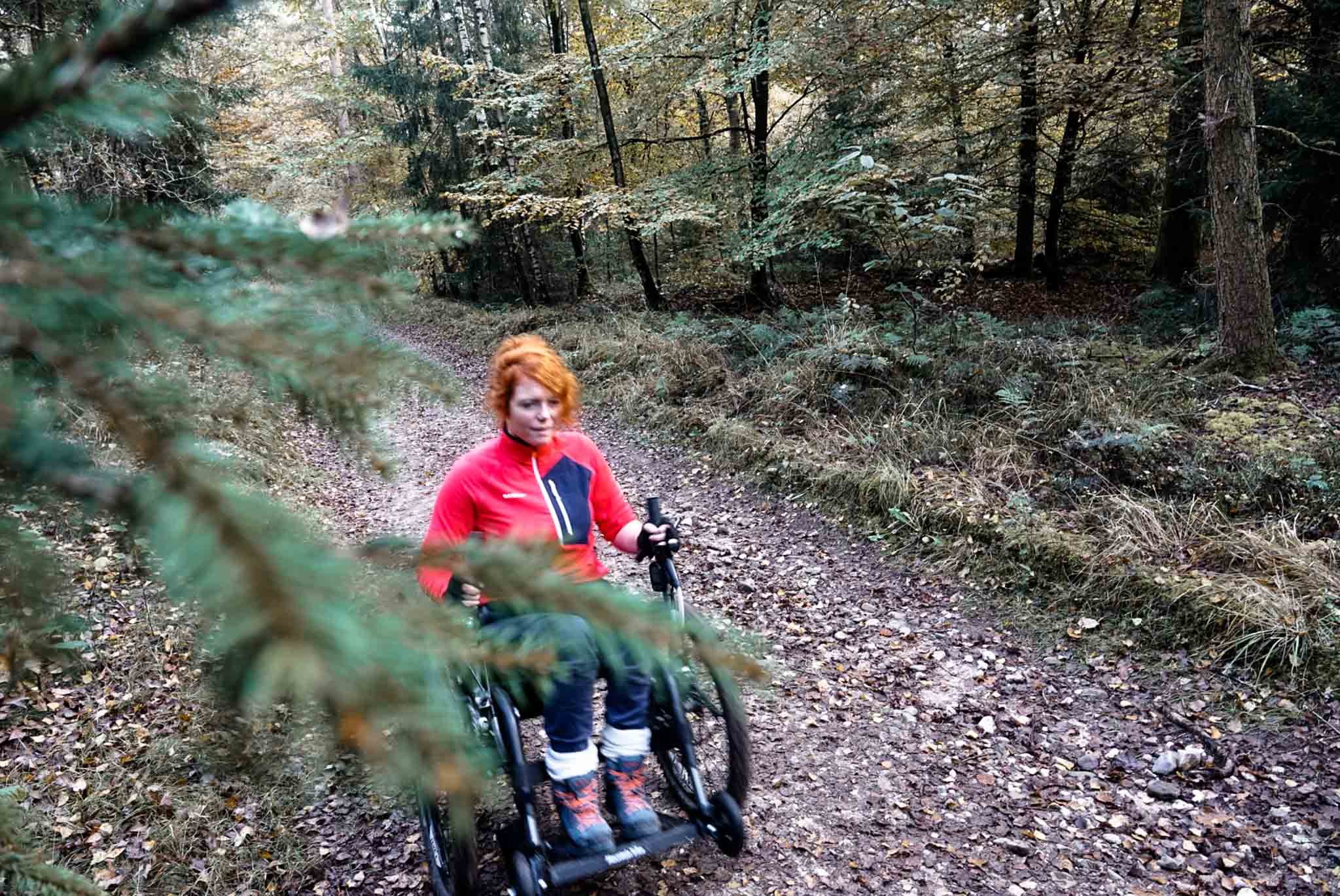 Persoon in een rolstoel op een boswandeling, omringd door bomen en herfstbladeren.