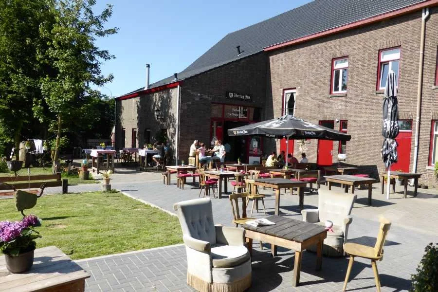 Buiten eetgelegenheid met tafels, stoelen en parasols voor een restaurant of café, met mensen die genieten van de zon.