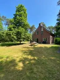 Toegankelijke accommodatie aan het Pieterpad. Een tuin met gras en grote bomen, een stenen huis met een houten deur en ramen.