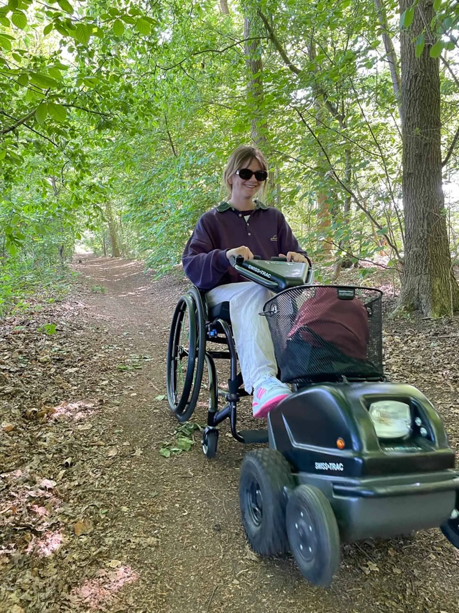 Vrouw in een rolstoel op een boswandeling, omgeven door groen bladerdak.