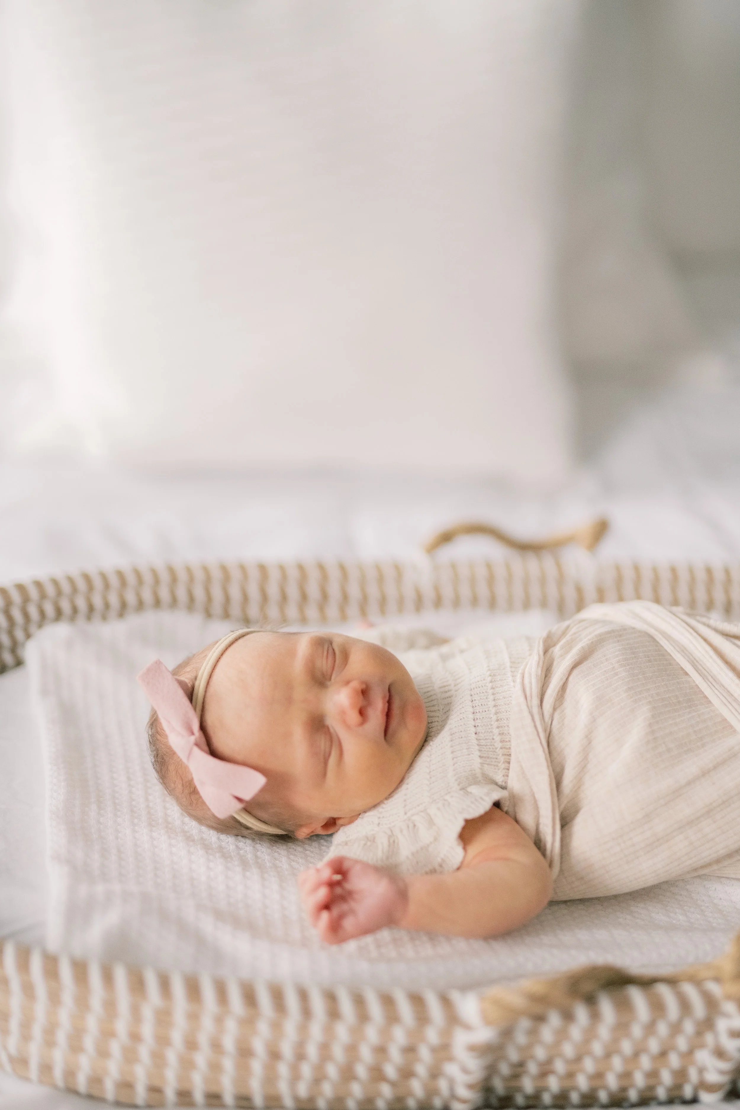 A sleeping baby girl with a pink bow headband, lying on her back in a wicker bassinet