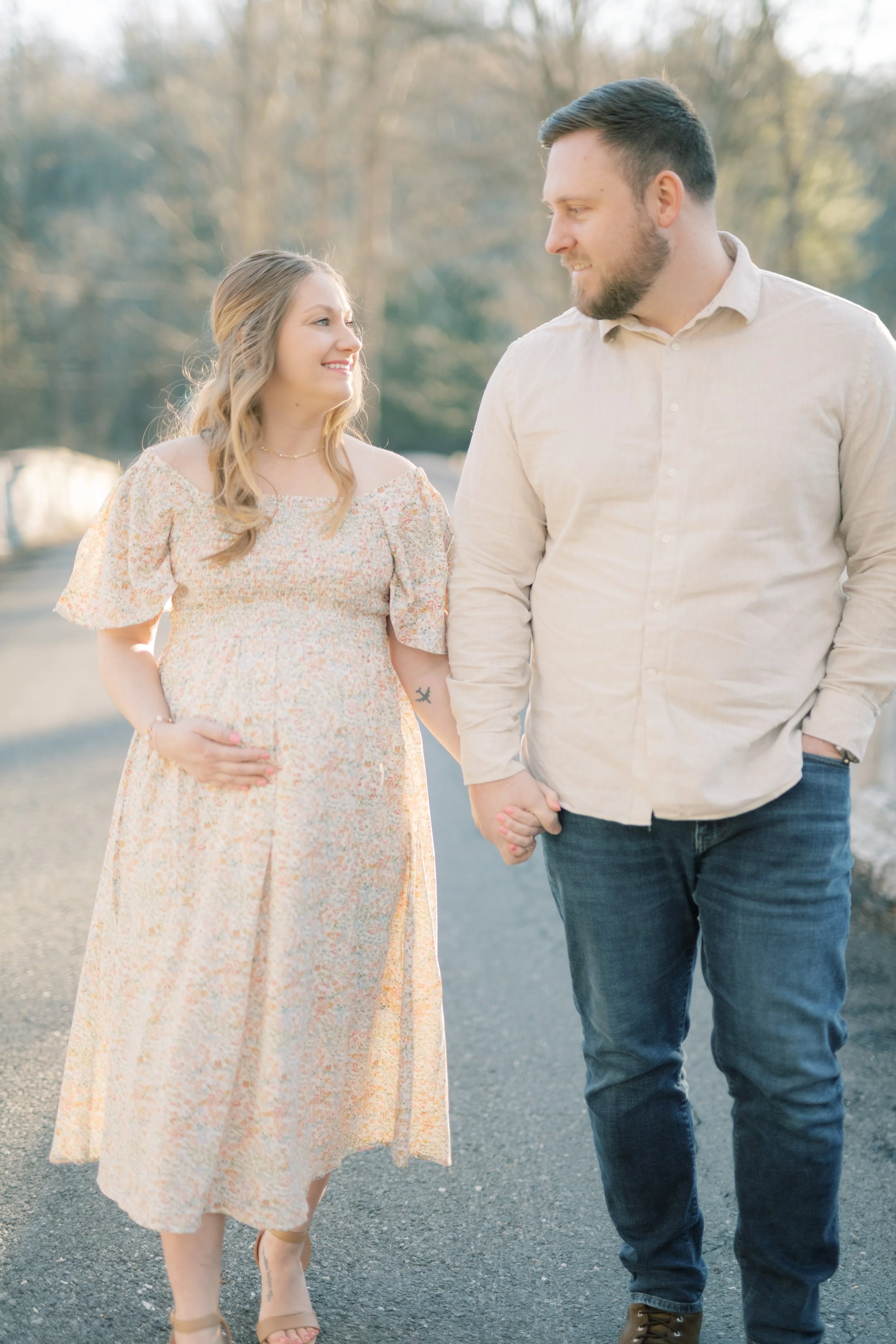 A couple holding hands walking outdoors in a park on a sunny day, with trees in the background.