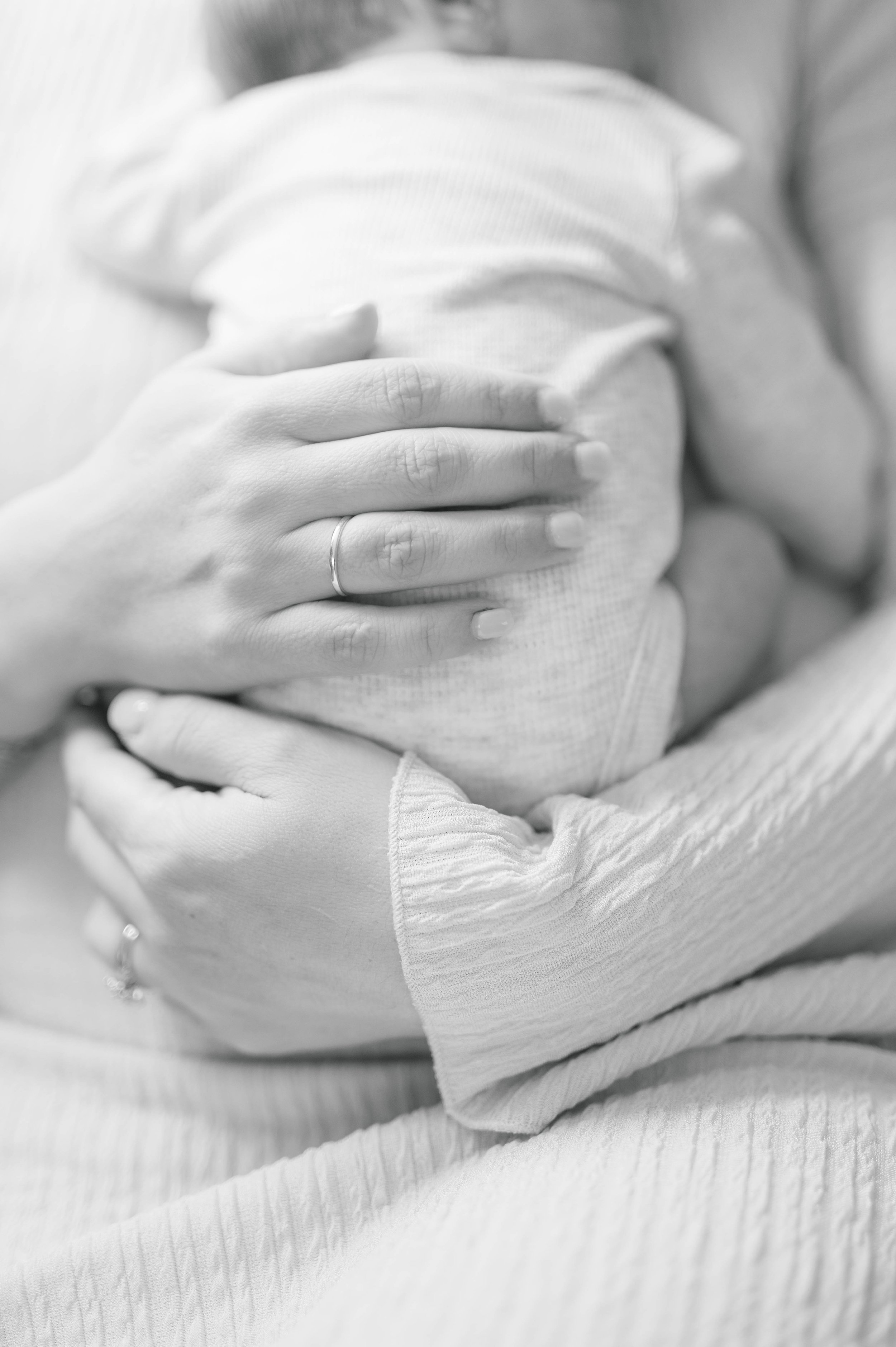 A person holding a newborn baby close to their chest, with their hand gently resting on the baby's back.