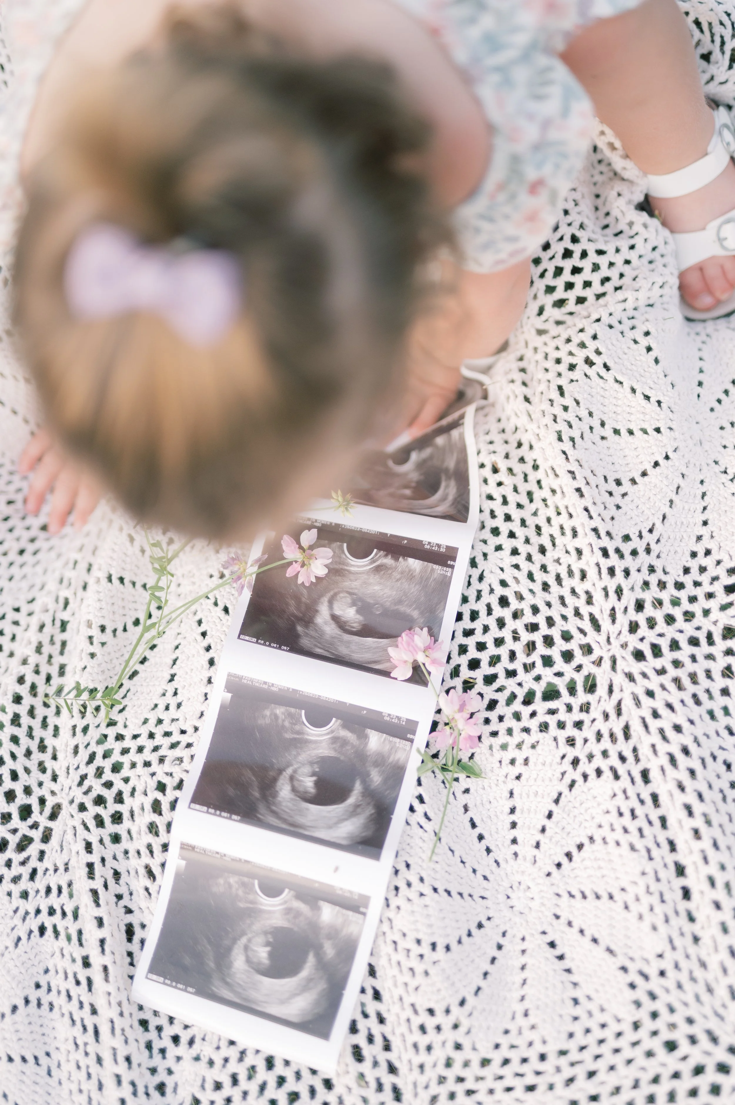 A young girl is looking at ultrasound pictures of a baby, placed on a crochet blanket decorated with pink flowers.