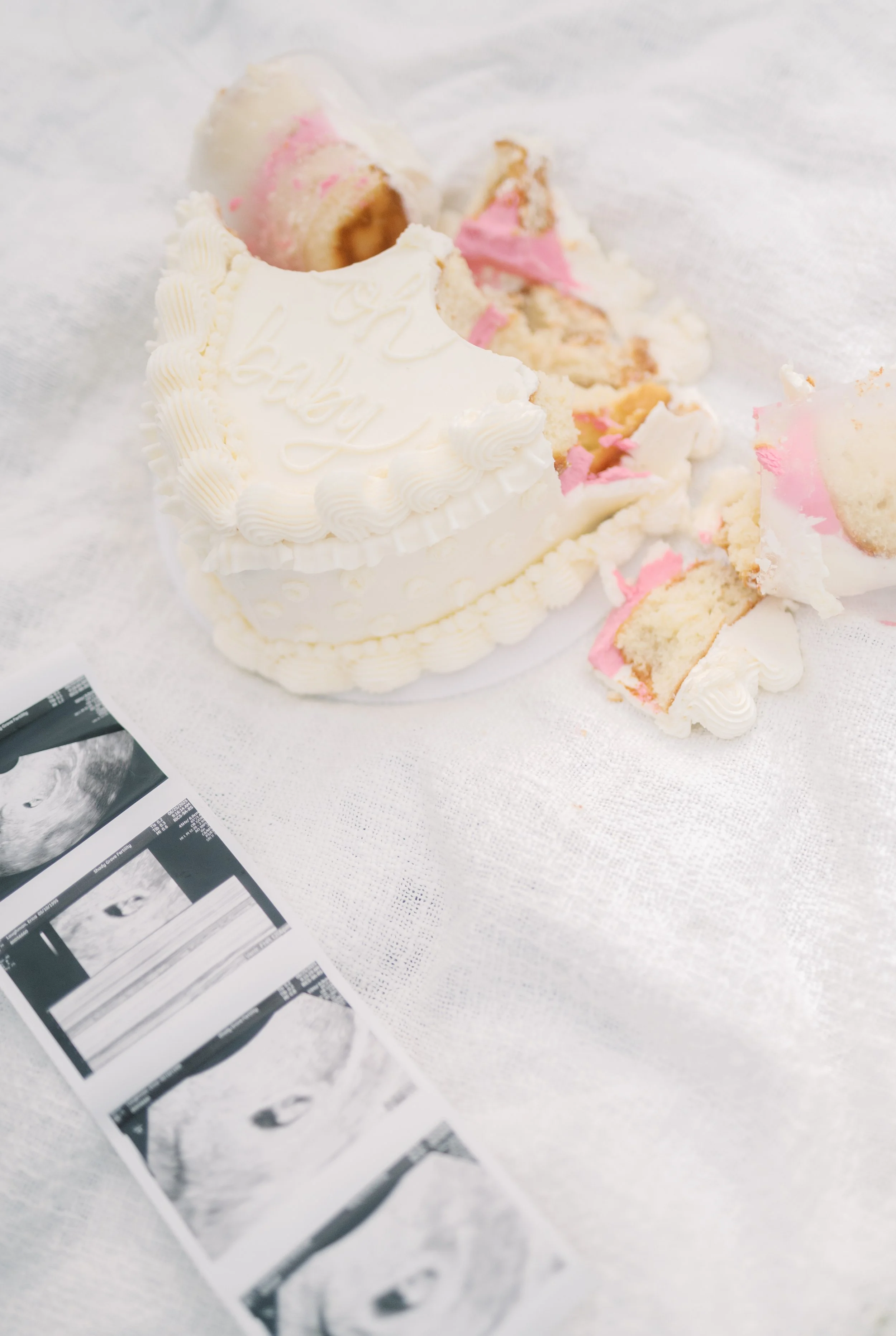 Broken white and pink frosted cake with layers of pink filling, placed on a white cloth, with ultrasound images scattered nearby.