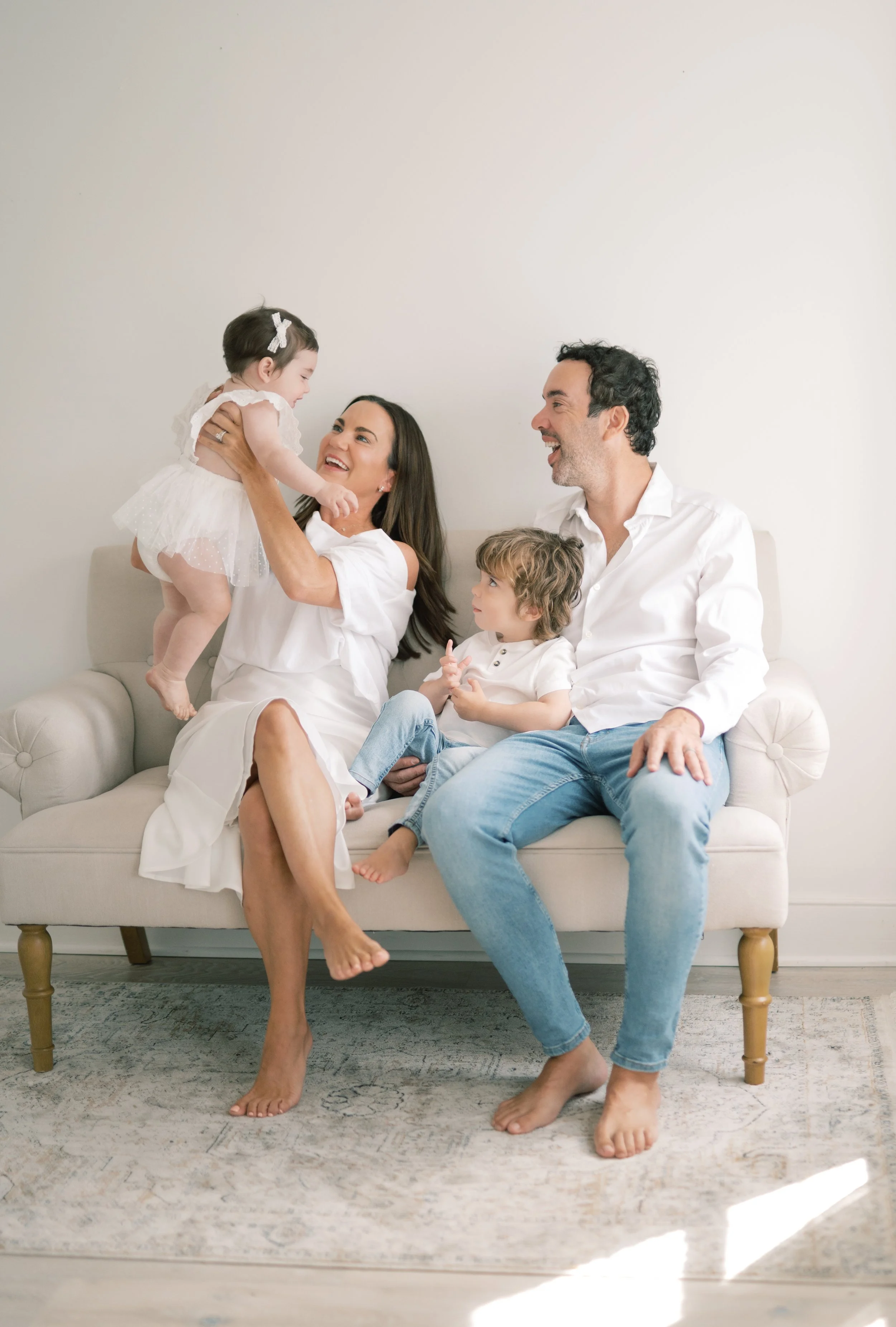 Happy family with two children and their parents sitting on a beige sofa in a bright minimalistic room, smiling and playing together.