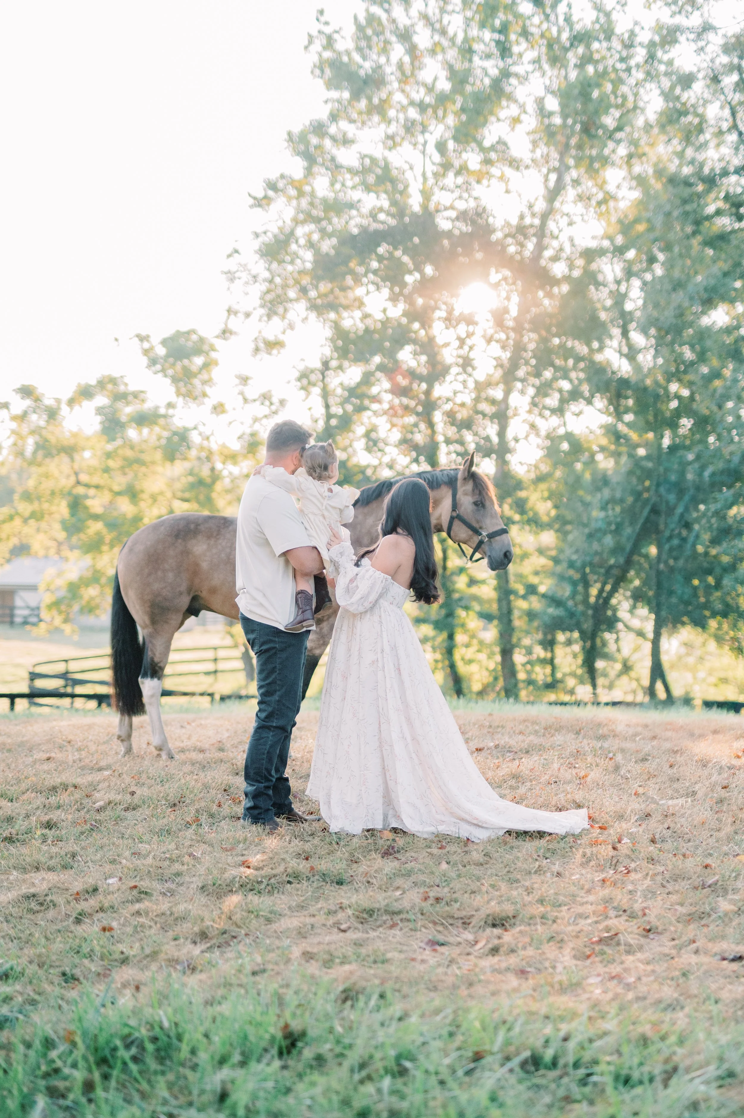 Family with a young girl and woman near a horse in a grassy field during sunset