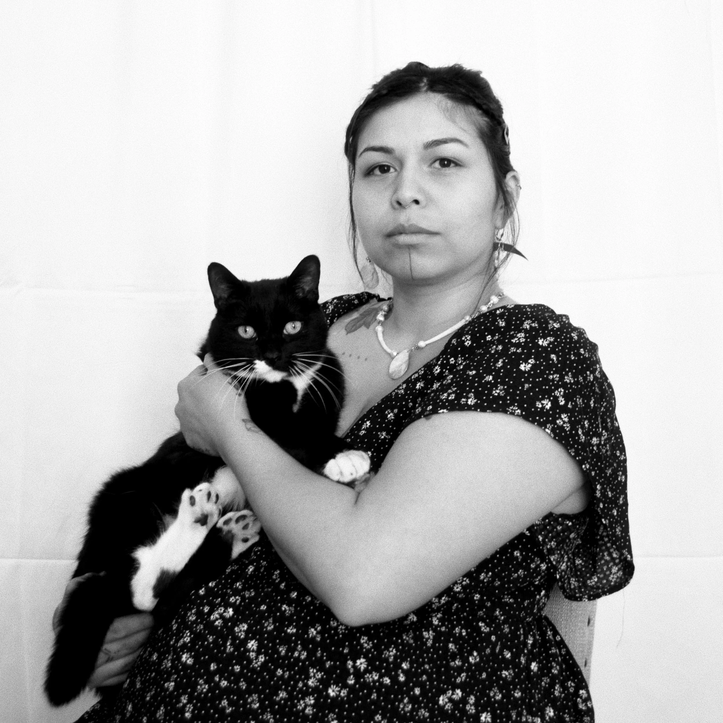 A black and white portrait of Atsei holding her tuxedo cat bongo. She is 7 months pregnant.